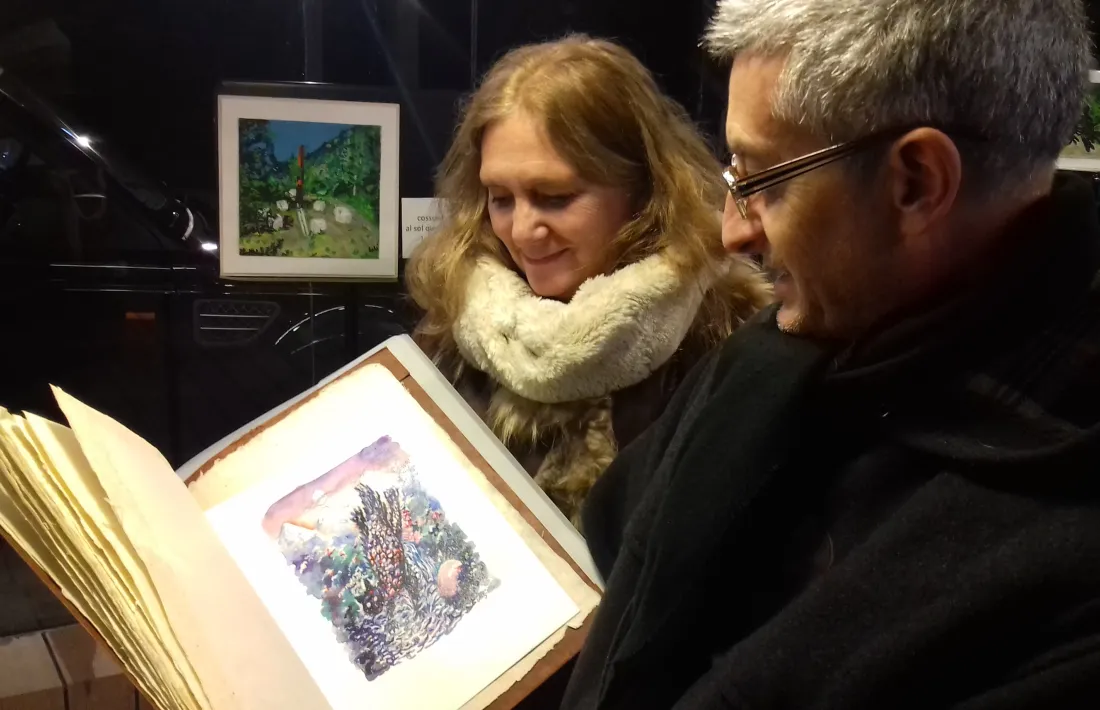 Loli Rodríguez i Manel Gibert contemplen els originals de Sergi mas per a ‘Al sol que bat la penya’. Al fons, aquarel·la de Rodríguez.