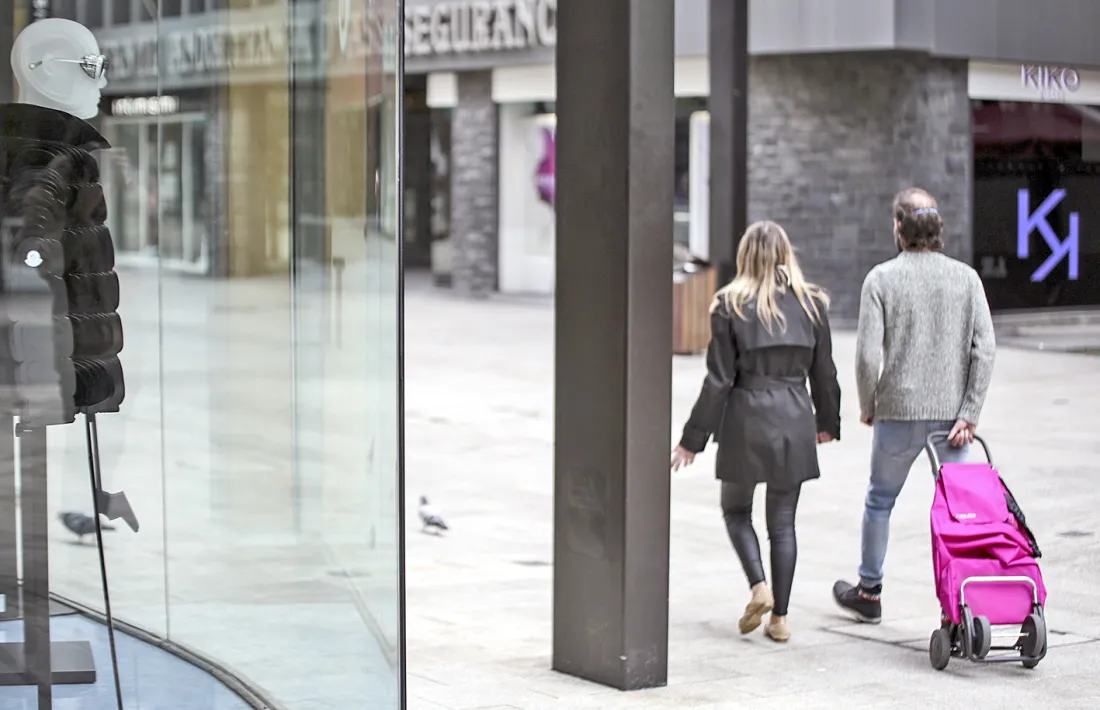 Dues persones passegen per l'avinguda Meritxell amb les botigues tancades.
