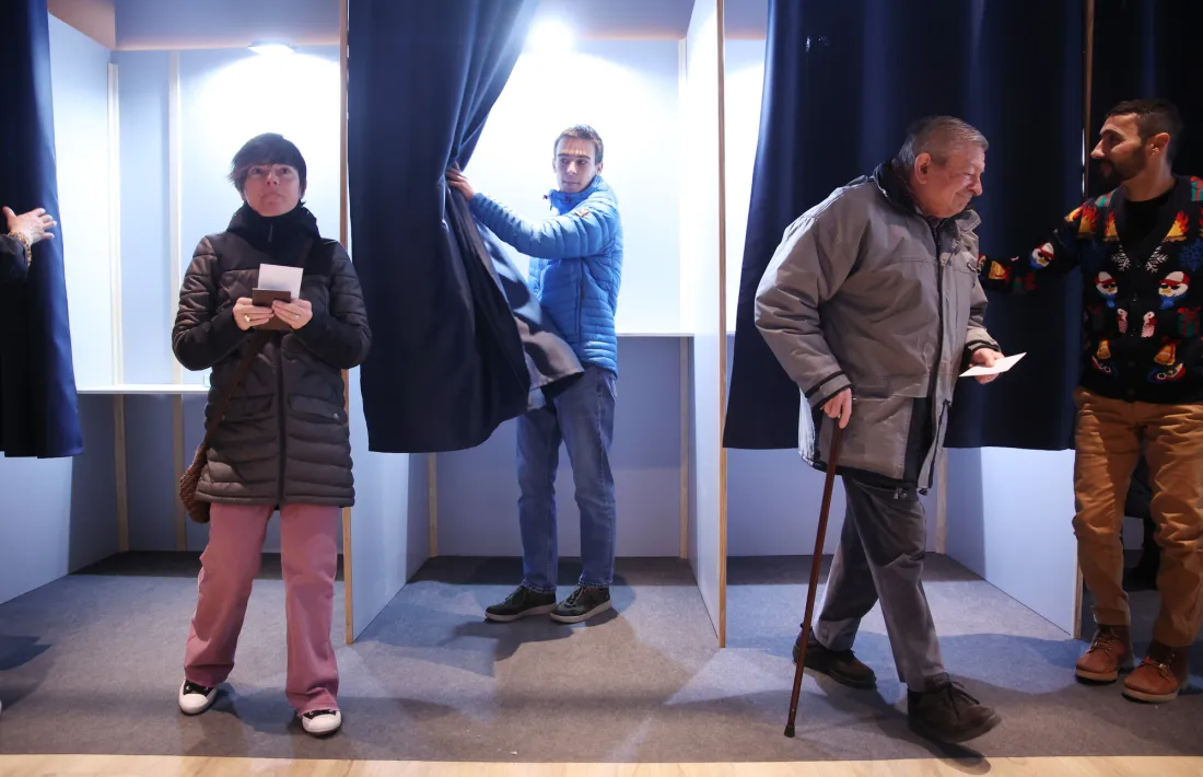 Diversos electors entrant i sortint de la cabina on hi havia les paperetes.