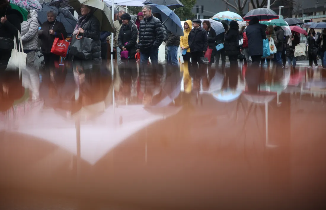 Persones fent cua sota la pluja per agafar el seu plat d’escudella.