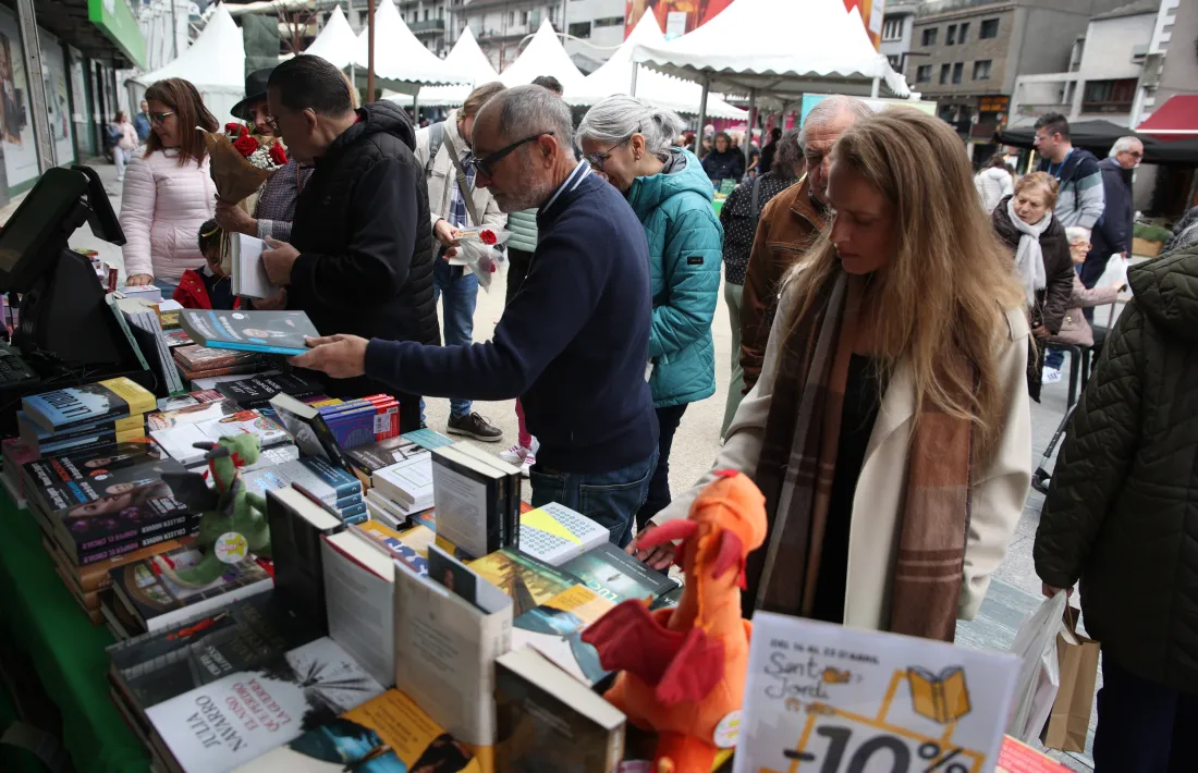 Dos homes i una dona miren llibres en una parada de la plaça de la Rotonda a Andorra la Vella.