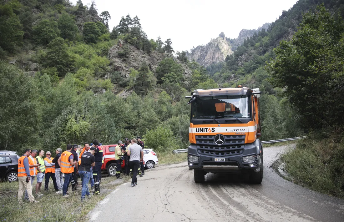 Un camió circula per la carretera d’Os de Civís mentre a l’esquerra hi ha una reunió entre tècnics.