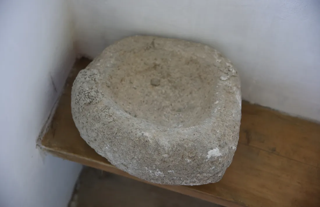 La pica per a l'aigua beneita, de granit i amb una cara gravada al costat.