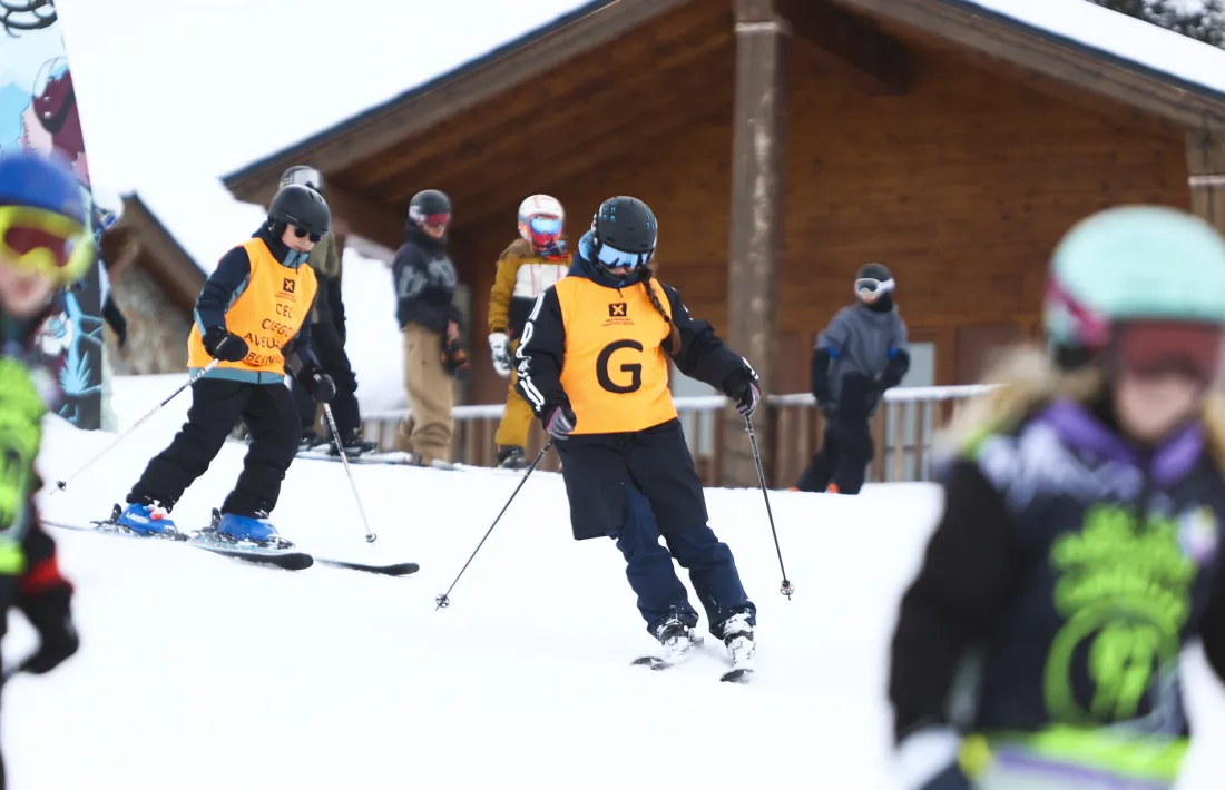 Amb peto taronja, en Marc, alumne, i la Mònica, monitora especialitzada, durant una classe d'esquí escolar.