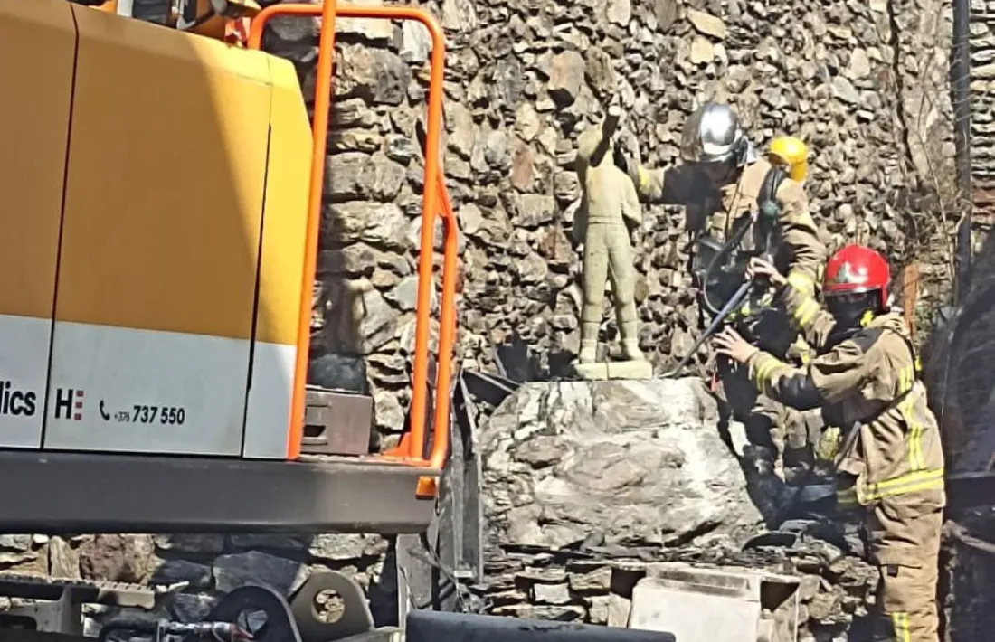 Un bomber retira la peça de bronze del sòcol, amb l'ajuda d'una excavadora.