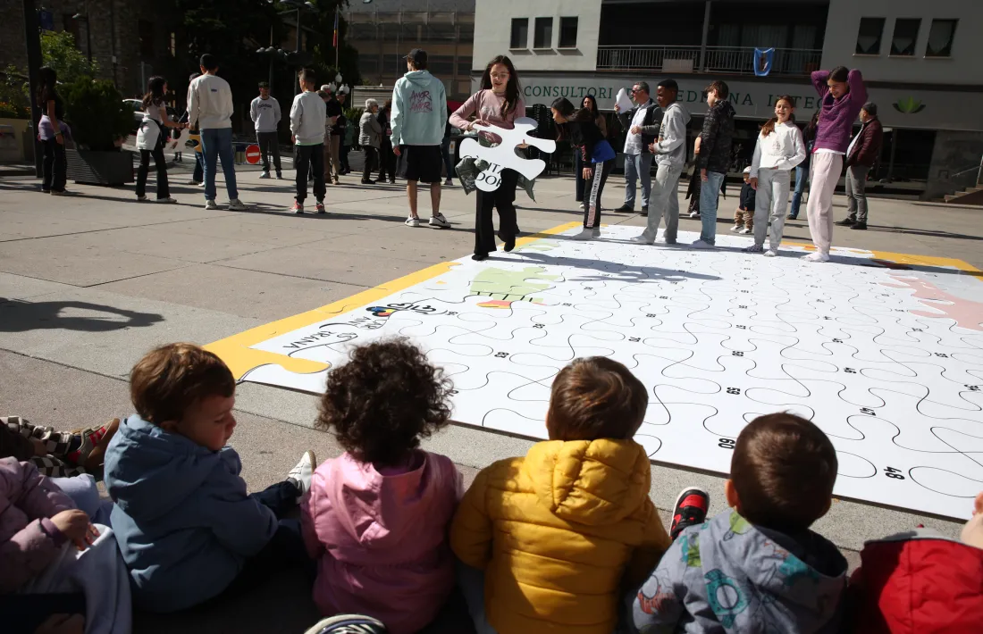 Una nena es disposa a col·locar una peça en el mural a Sant Julià de Lòria.